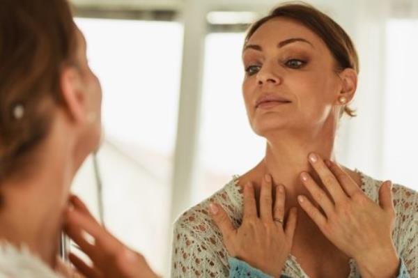 allergic reaction to the vaccine Headshot of mature woman checking her wrinkles and line ex<em></em>pressions on her skin of her neck in front of a mirror.