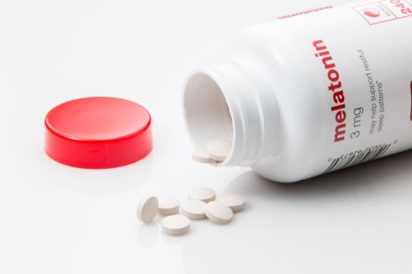melato<em></em>nin supplements spilled out of bottle on white background