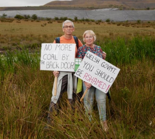 Chris and Alyson Austin stand with protest placards on the hillside next to the perimeter of the Ffros Y Fran open cast coal mine. They live within 300 metres of the Ffos-y-Fran opencast mine in the Dowlais estate, Merthyr, south Wales.