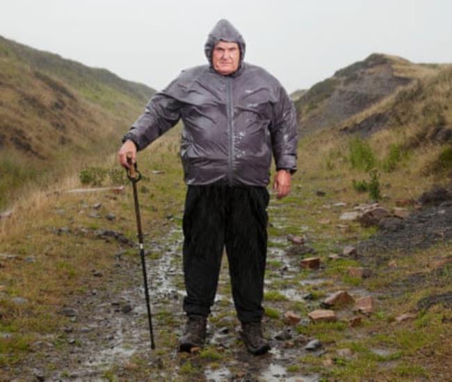 Retired coalminer Phil Duggan on a hillside in a raincoat with a walking stick