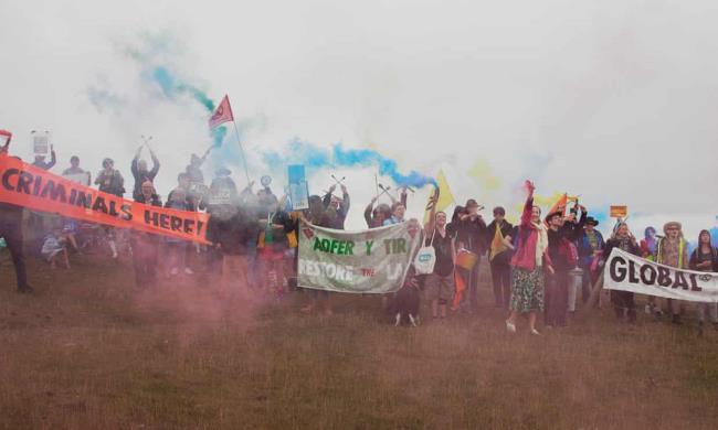 Four campaigners holding a pink banner saying ‘stop illegal coal, restore the land’ on a road at the top of the mine with other protesters behind them